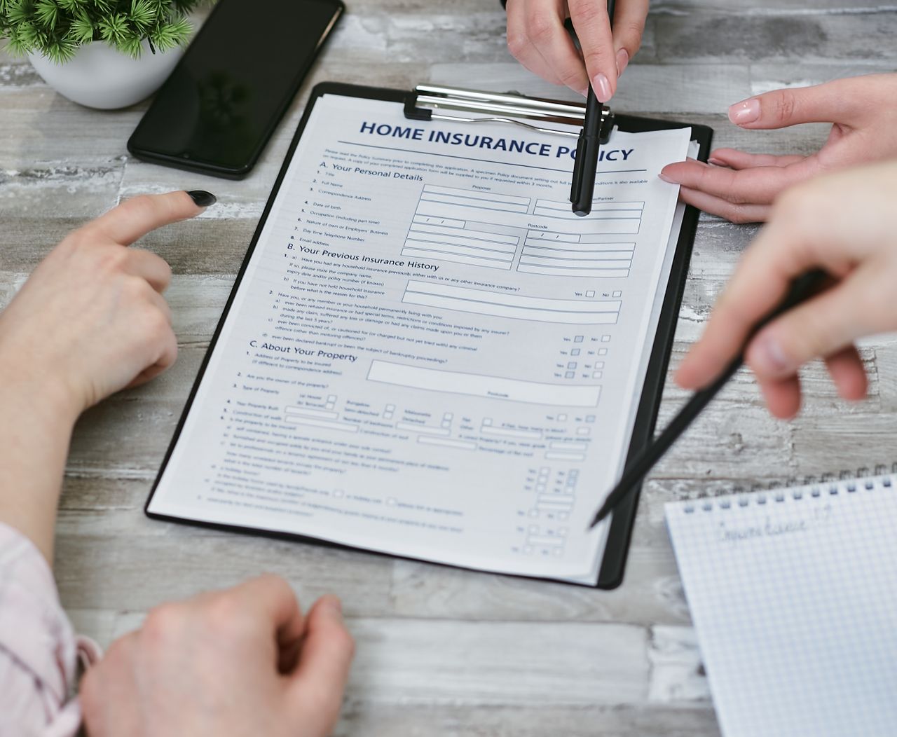 services-01 Three individuals collaborating on a home insurance policy document. Elements include a clipboard, notes, and pointing hands.